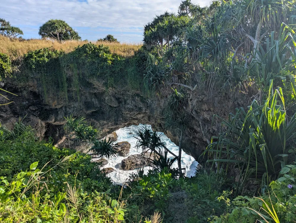A natural limestone sea arch surrounded by tropical greenery at Hufangalupe